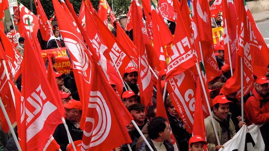 La foto mostra una manifestazione sindacale con una folla compatta di manifestanti che sventolano numerose bandiere rosse della CGIL e della FILLEA, la categoria del sindacato che rappresenta i lavoratori dell’edilizia, del legno e dei materiali da costruzione. I partecipanti indossano cappellini rossi con il logo CGIL, creando un forte impatto visivo e cromatico. L’inquadratura mette in evidenza il senso di unità e determinazione del gruppo, evocando una mobilitazione compatta e decisa a difendere i diritti dei lavoratori. Sullo sfondo si intravedono striscioni e altri simboli legati al mondo sindacale.